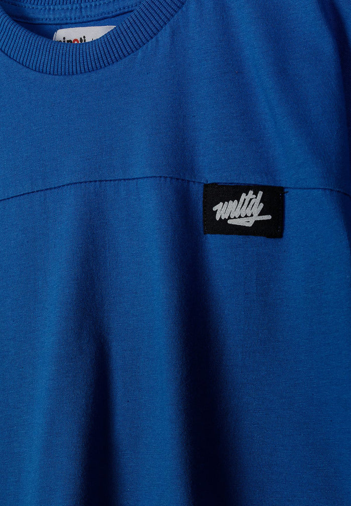 Detail of a royal blue t-shirt with a round neck and logo badge.