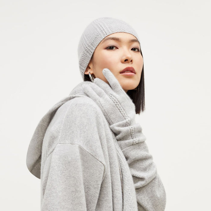 Side image of a woman standing wearing the Circle Cable Beanie—Cashmere in Heather Gray | Exclude