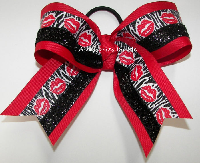 A red and black hair bow with a black elastic loop, featuring red and black glitter stripes, red lips on a zebra print, and solid red borders. A watermark 'Attibories by Me' is visible across the center.