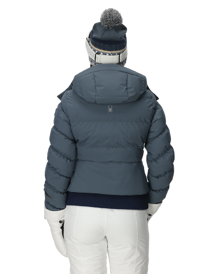 Person wearing a blue puffer jacket and white pants on a white background