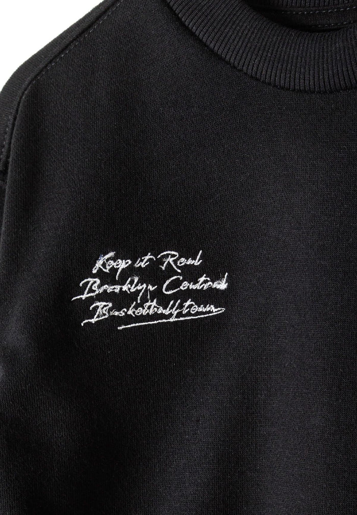 Detail of a black boys' sweatshirt featuring a graphic print and ribbed neckline.