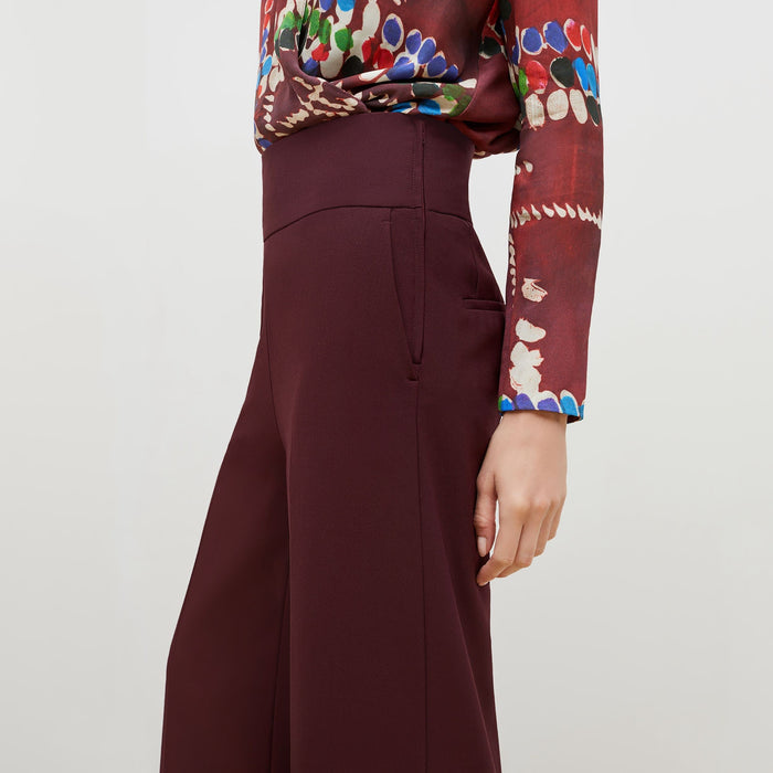 Side detail image of a woman standing wearing the Hadley Pant-Sharkskin in garnet