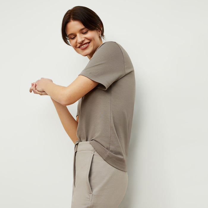 Side image of a woman standing wearing the Leslie T-Shirt—Compact Cotton in Pebble