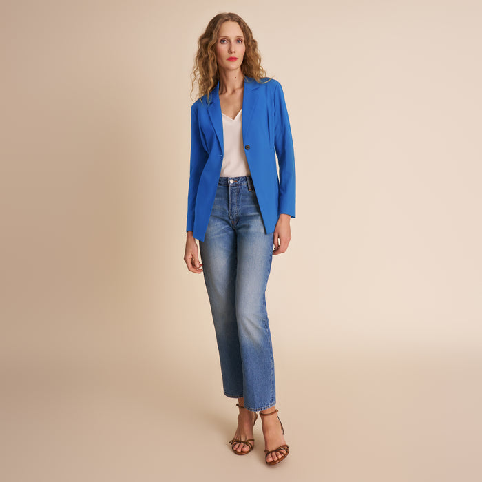Woman wearing a blue blazer and jeans on a beige background