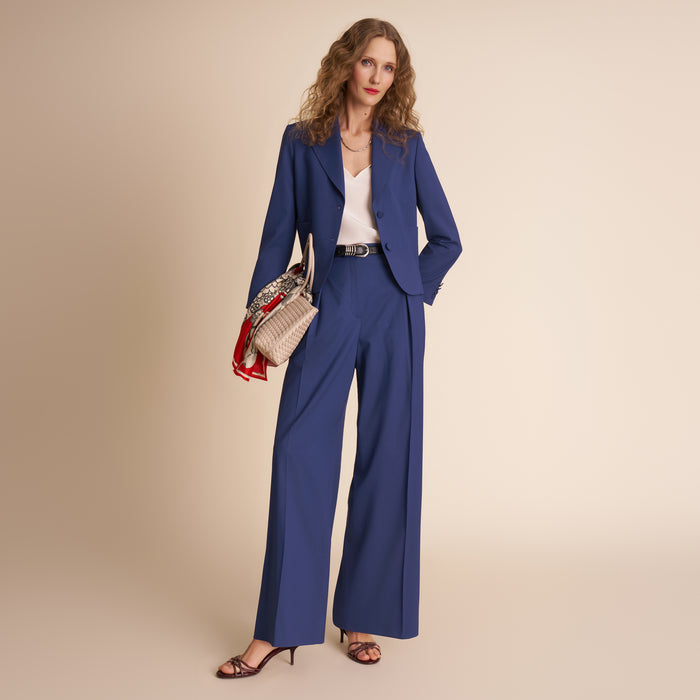 Woman wearing a blue suit with a beige background.