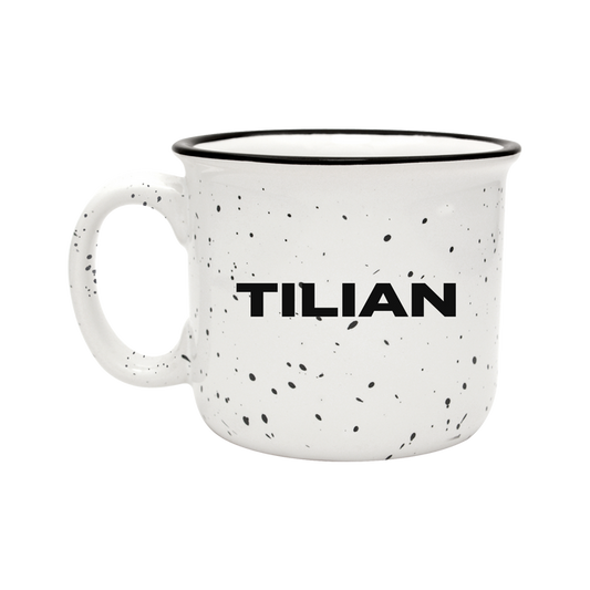 A white ceramic mug with black speckles features the Tilian brand name in bold black letters on the side, set against a solid black background.