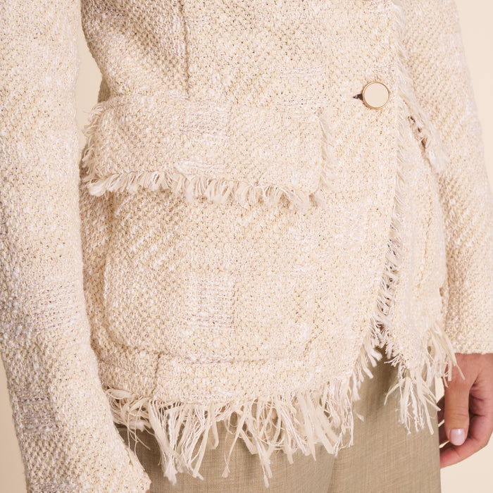 Close-up of a textured beige sweater with fringes and a button.