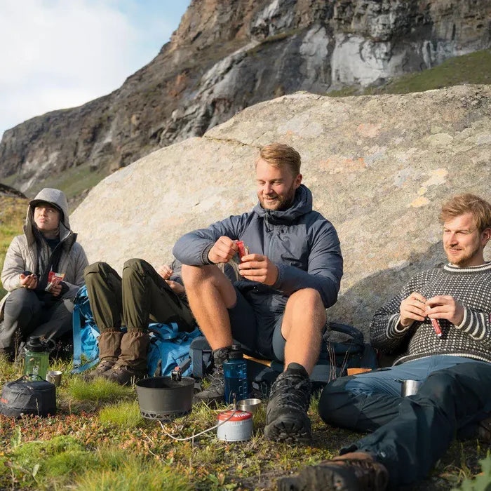 Three people sitting outdoors in a mountainous area, preparing food with a Primus Express Spider Camping Gas Stove
