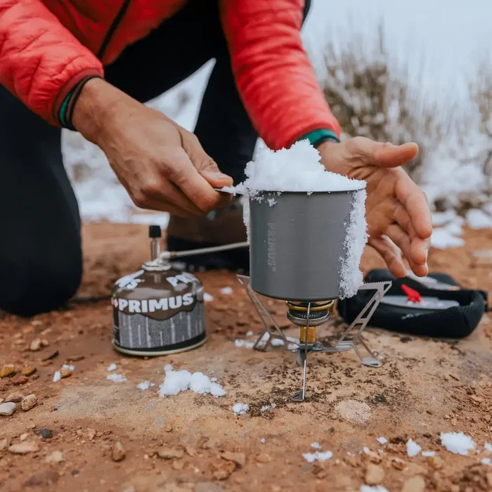 Person using a Primus Express Spider Camping Gas Stove with a pot to melt snow on wintry ground