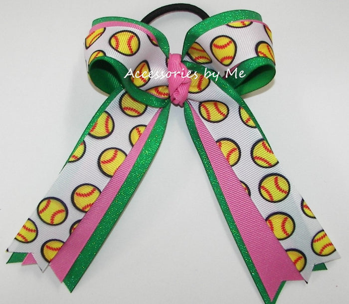 A hair bow accessory with a black elastic band, featuring a white ribbon printed with yellow and red softball patterns, green glitter trim, and pink ribbon accents. A watermark reading 'Accessories by Me' is visible across the center.