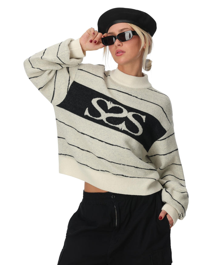 Person wearing a white sweater with black text and black pants on a white background